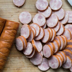 Sliced sausages and whole sausages on a wooden board with a knife and bell pepper. Ideal for culinary context.