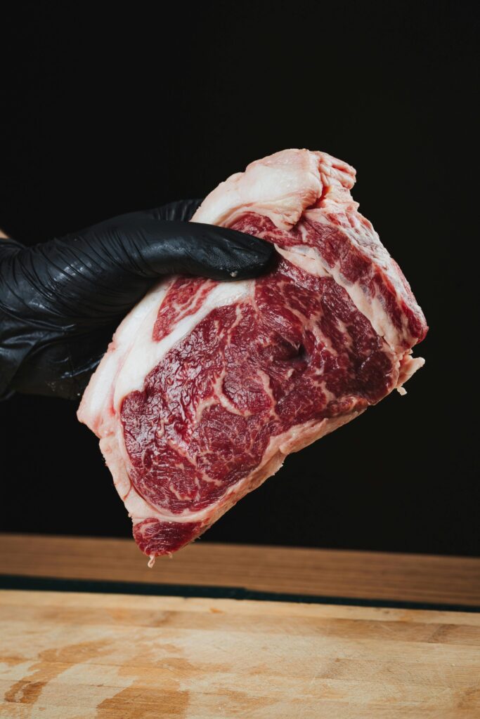 Close-up of a raw ribeye steak held by a gloved hand on a wooden surface.