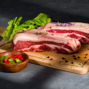 Close-up of raw beef ribs on cutting board with herbs and spices, perfect for cooking enthusiasts.