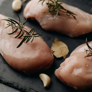 Close-up of raw chicken breasts with rosemary and bay leaves on slate.