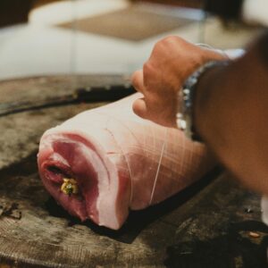 Close-up of a chef's hand seasoning raw pork on a rustic wooden block.